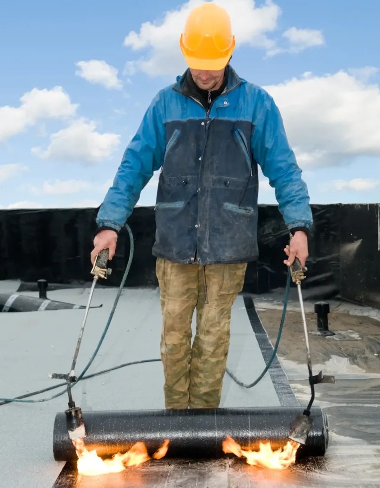 ASI Construction worker working on installing a flat roof on a commercial building using proper tools to install