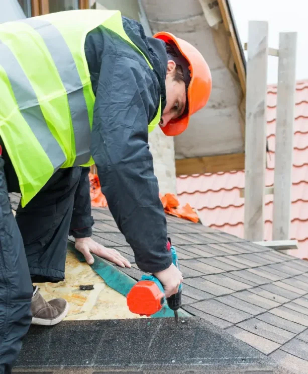ASI Construction worker on roof with proper safety equipment installing shingles on a roof